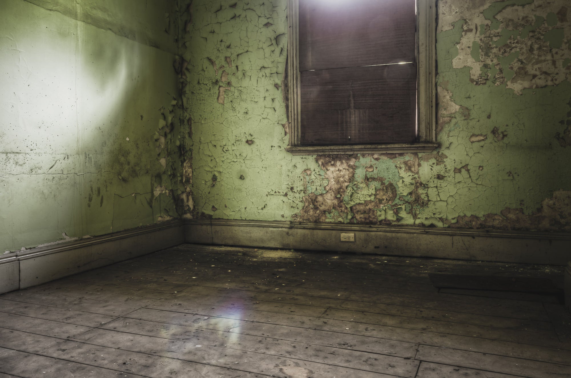 Bare Guest Room at Terminus Hotel, light seeps in through a boarded window, casting a dull glow across the floorboards.