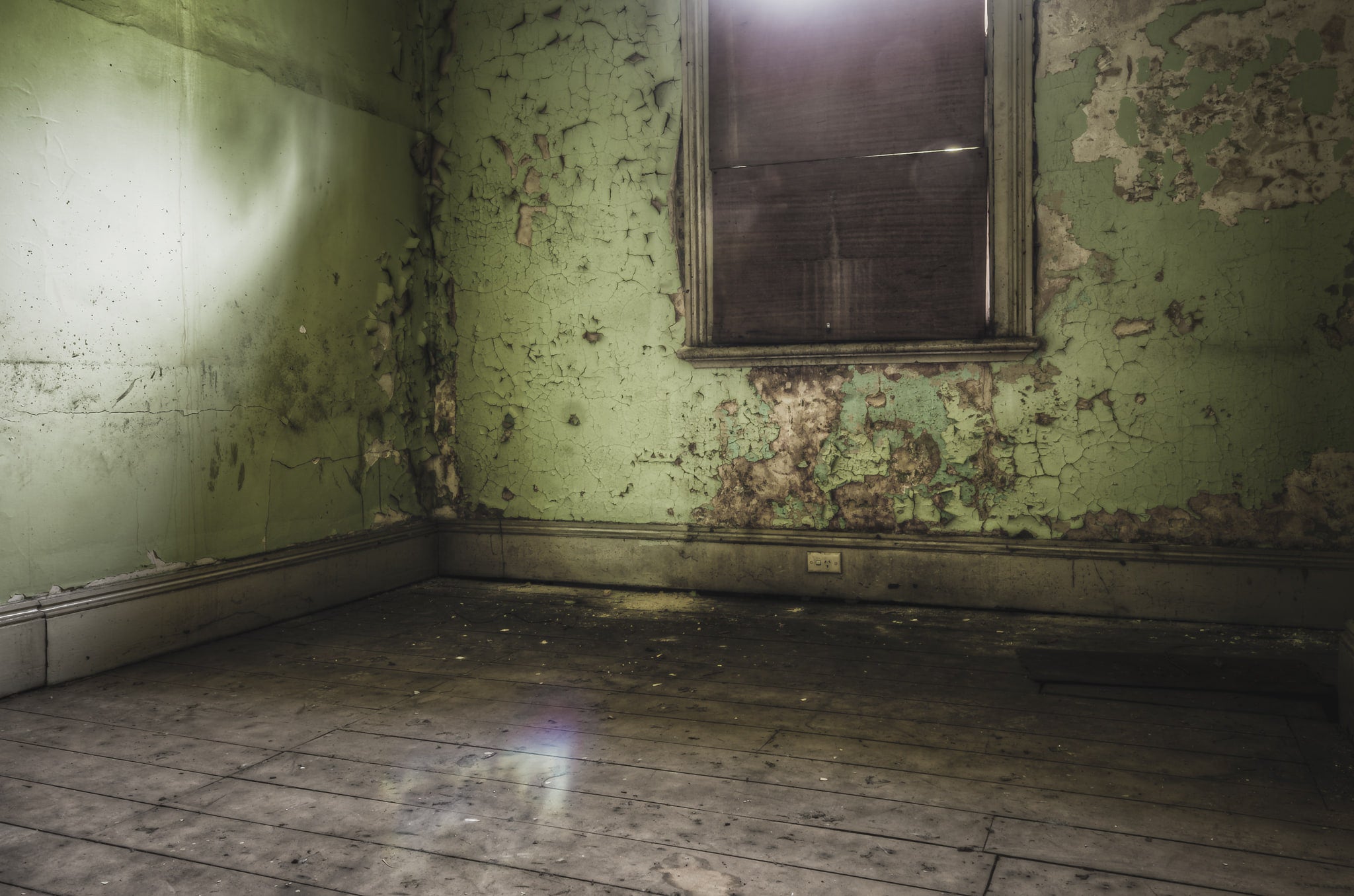 Bare Guest Room at Terminus Hotel, light seeps in through a boarded window, casting a dull glow across the floorboards.