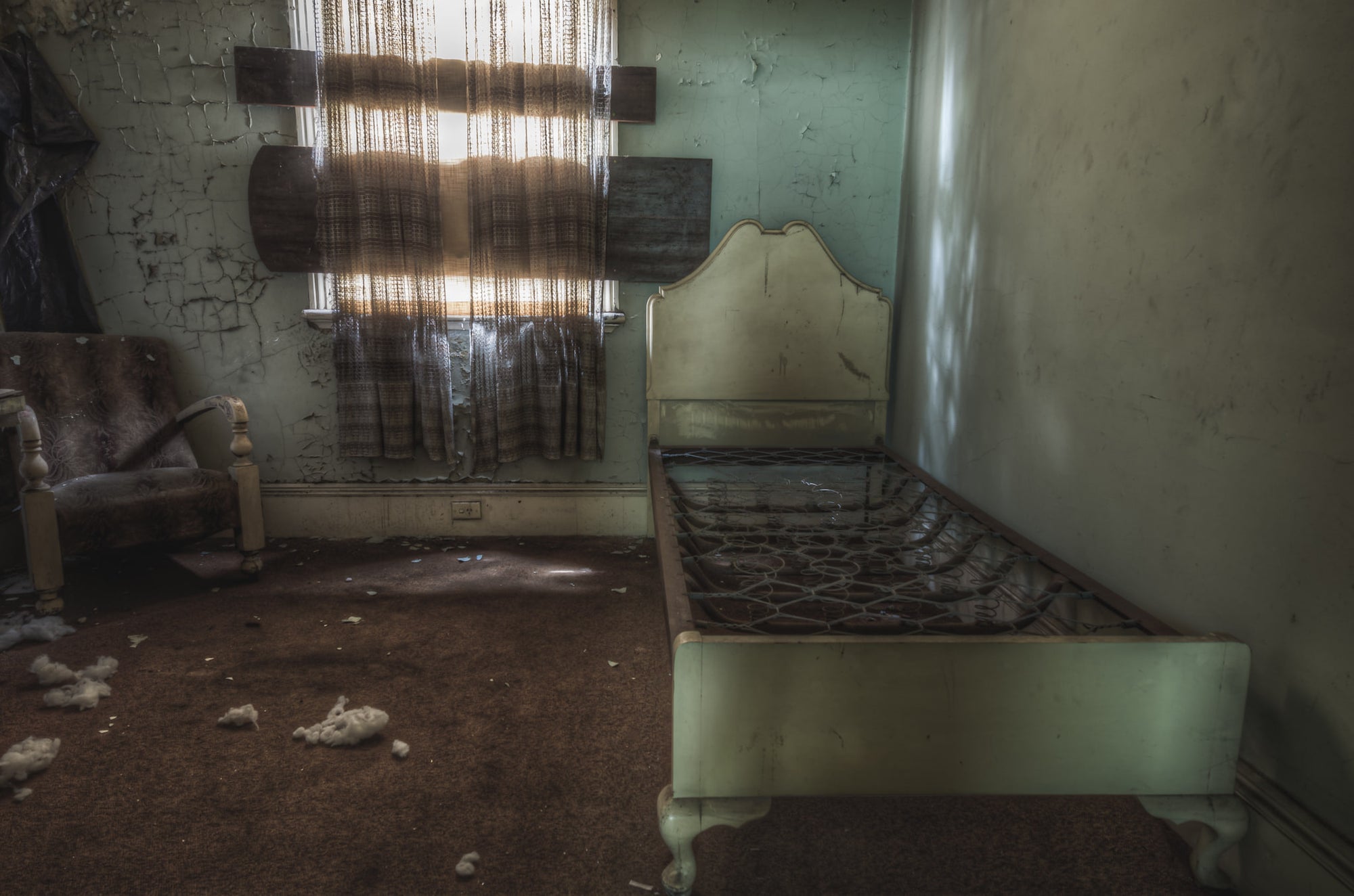 Guest Room at Terminus Hotel, a single bed frame sits along the wall, its bare springs exposed, beside a worn armchair.