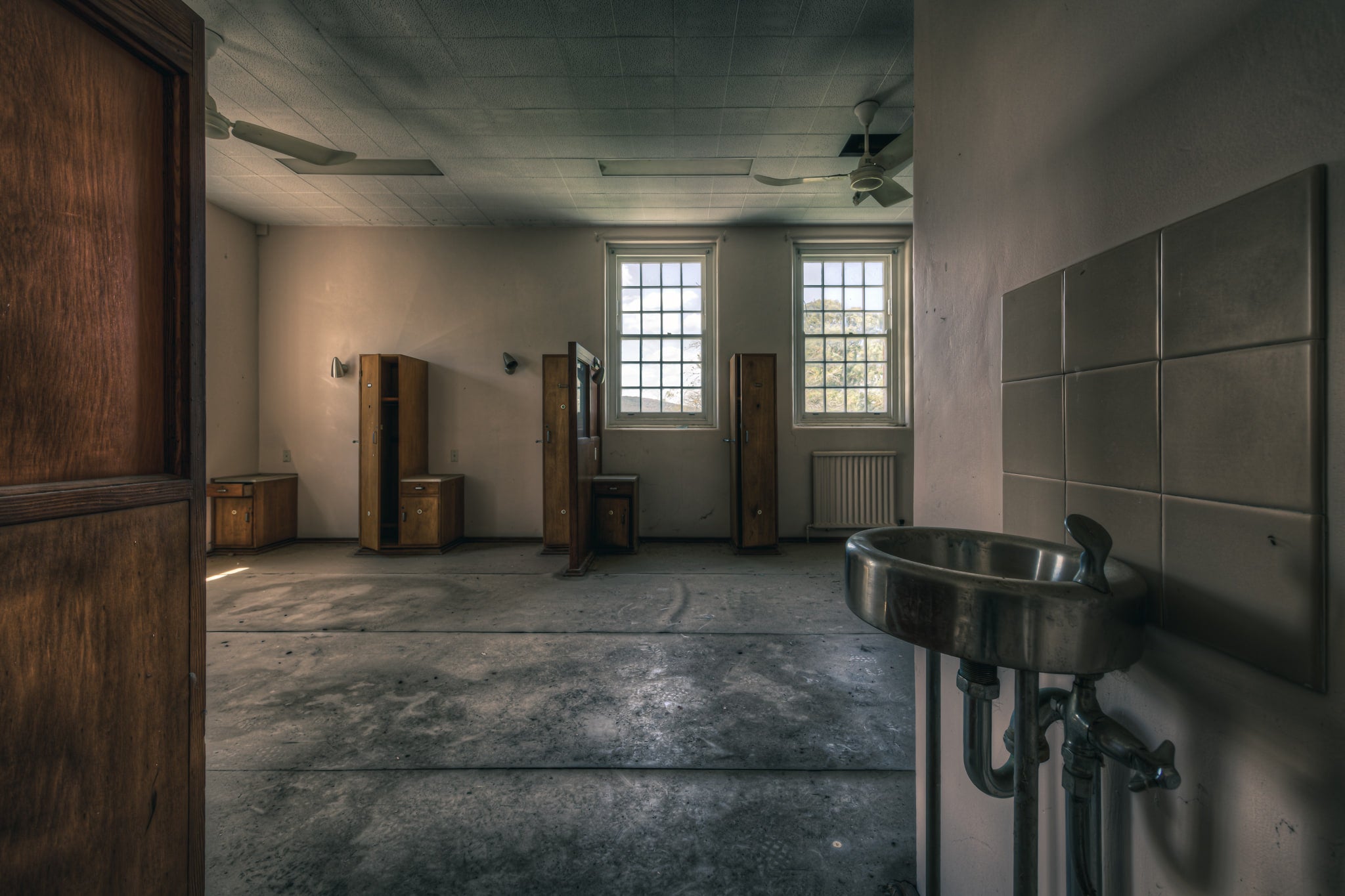 Bubbler at The Asylum, a stainless steel bubbler sits mounted against square ceramic tiles, its chrome pipework exposed.