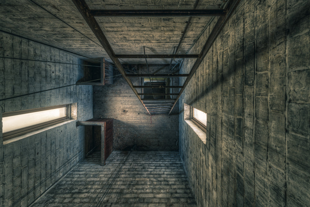 Clocktower Ladders at The Asylum, rough concrete block walls rise vertically on all sides, narrowing toward a steel ladder.