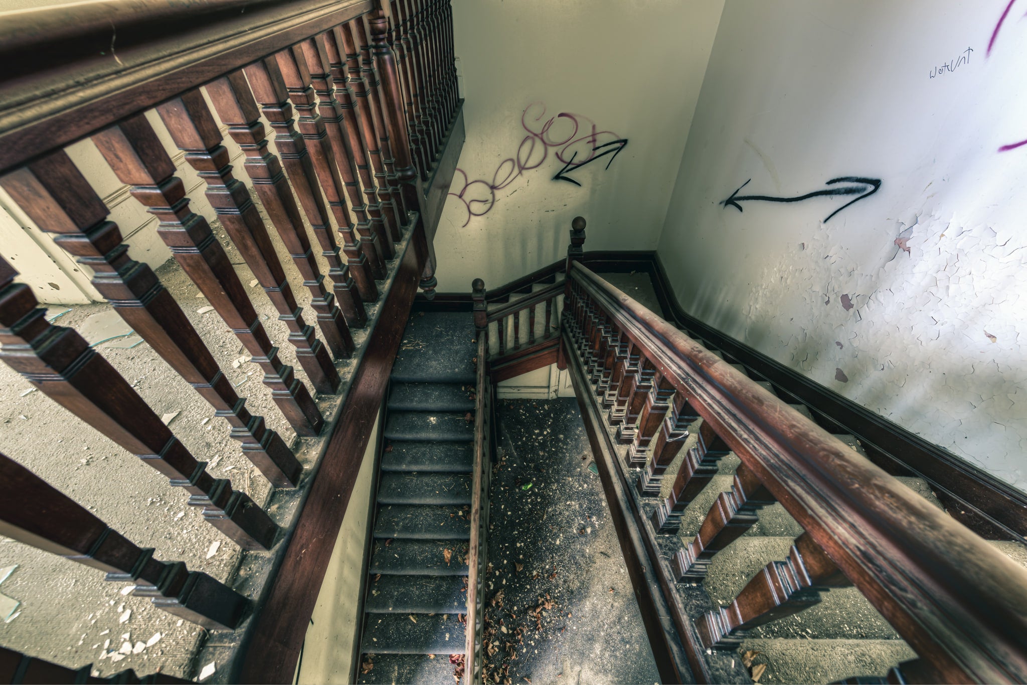 Decayed Stairwell at The Asylum, dark timber balusters run in tight rows down a multi-storey stairwell, their turned.