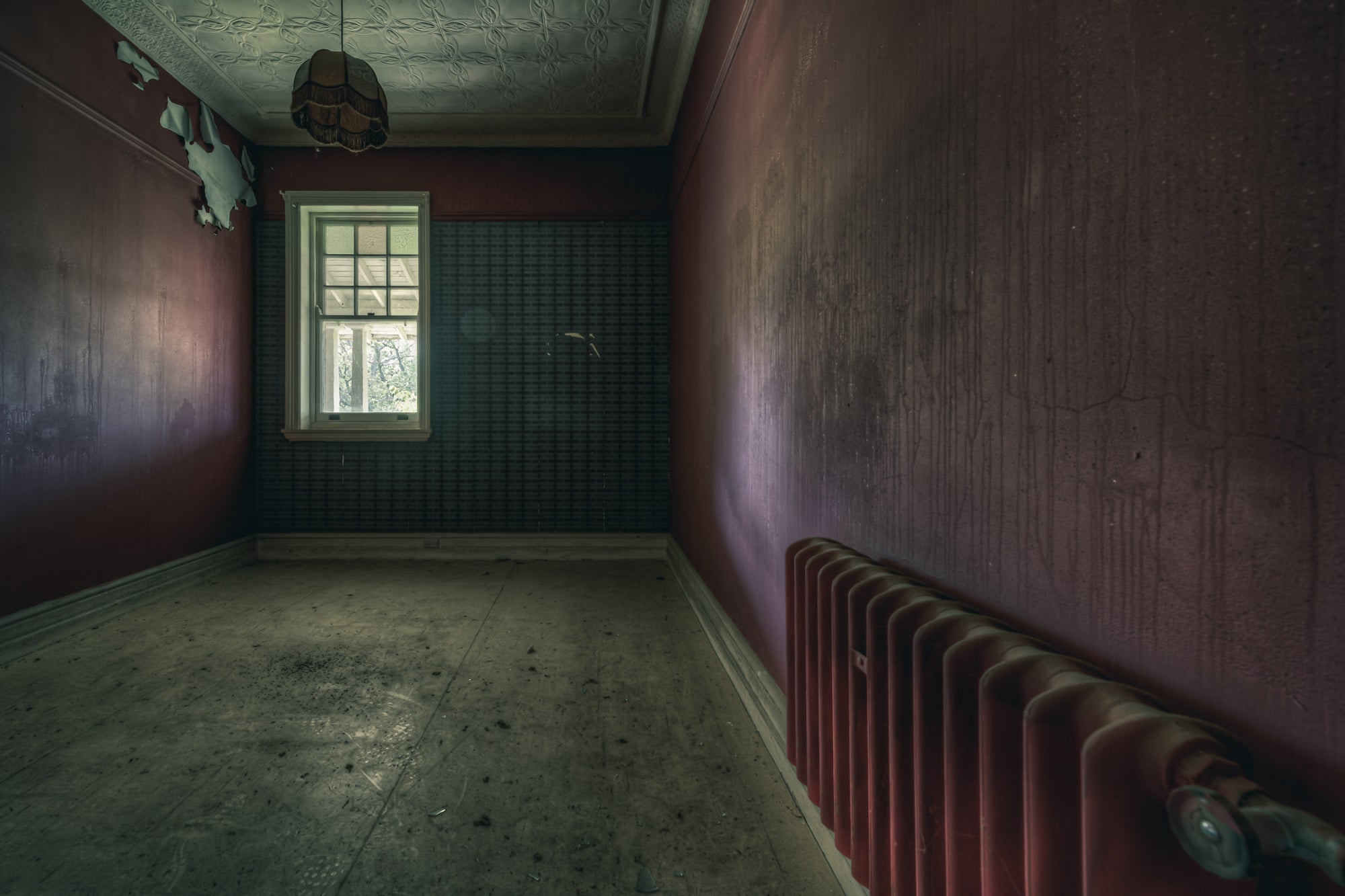 Heater at The Asylum, a cast-iron column radiator sits against the far wall, painted the same deep oxblood as the room.