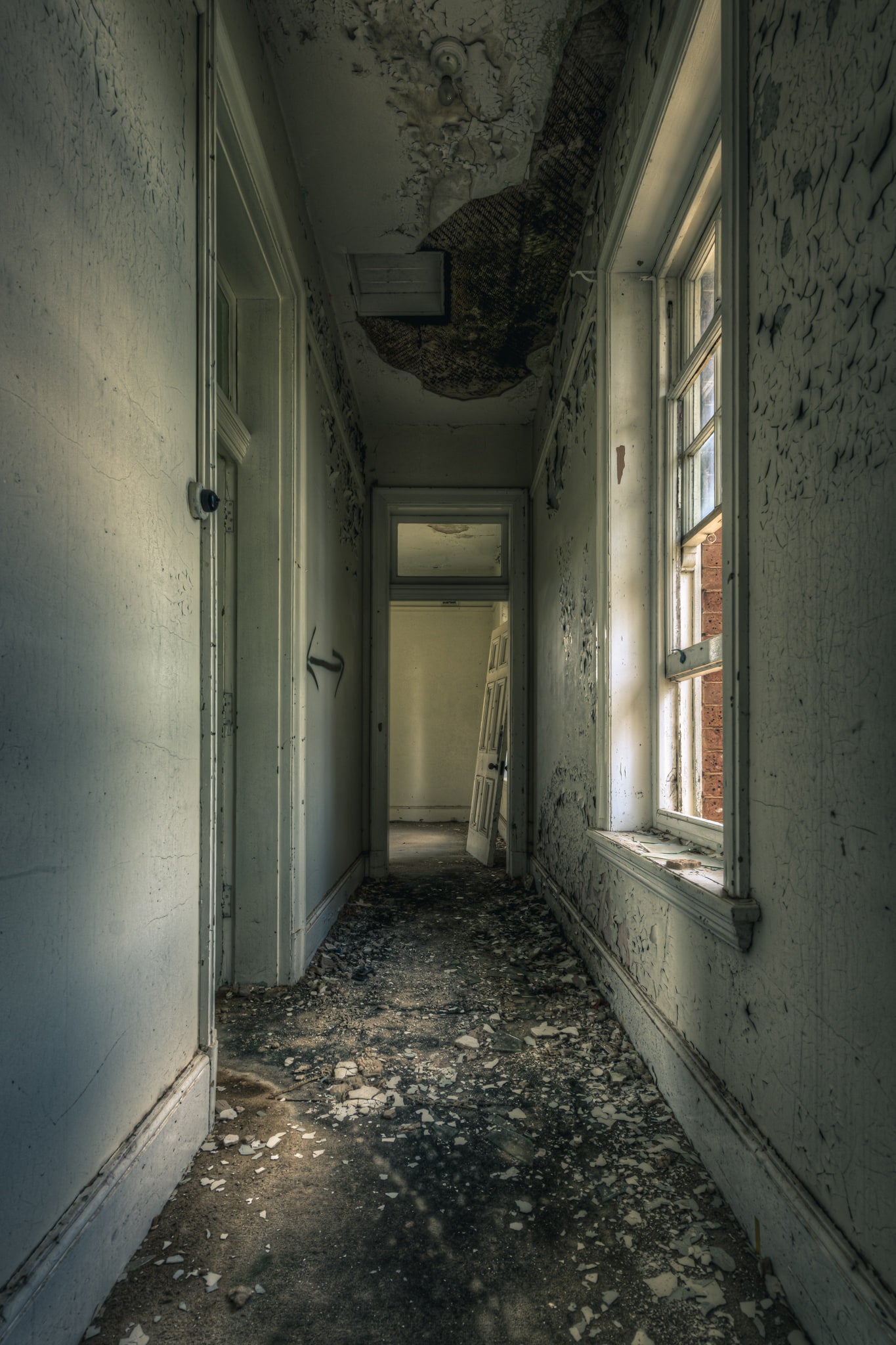 Mouldy Hall at The Asylum, a narrow corridor runs toward an open doorway at the far end.