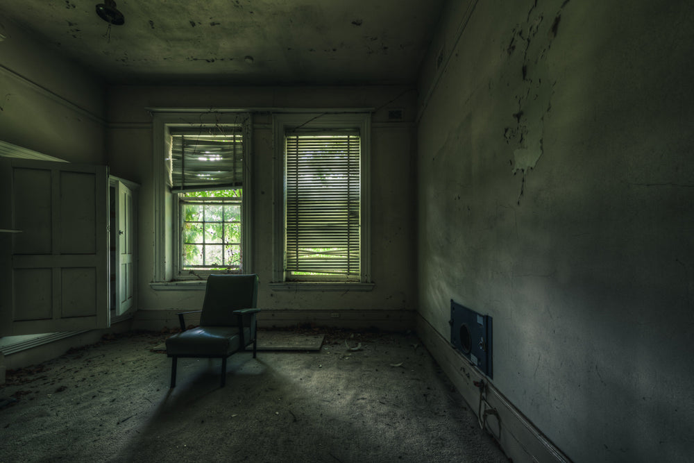 Slots of Light at The Asylum, a single vinyl chair sits near two windows in an otherwise empty room.