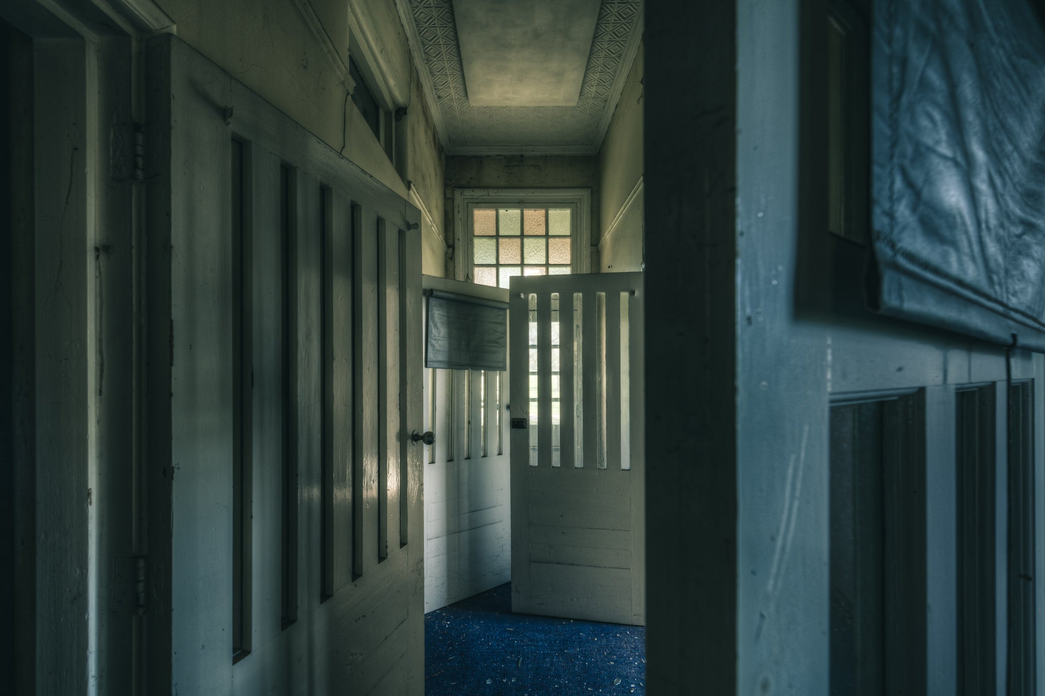 Slotted Doors at The Asylum, a narrow corridor lined with tall timber doors, each cut with vertical slotted openings.