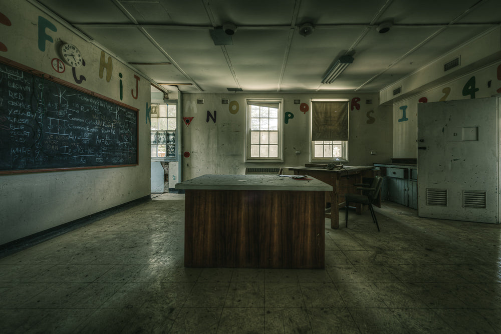 Teaching Table at The Asylum, a heavy timber desk sits at the centre of a disused classroom.