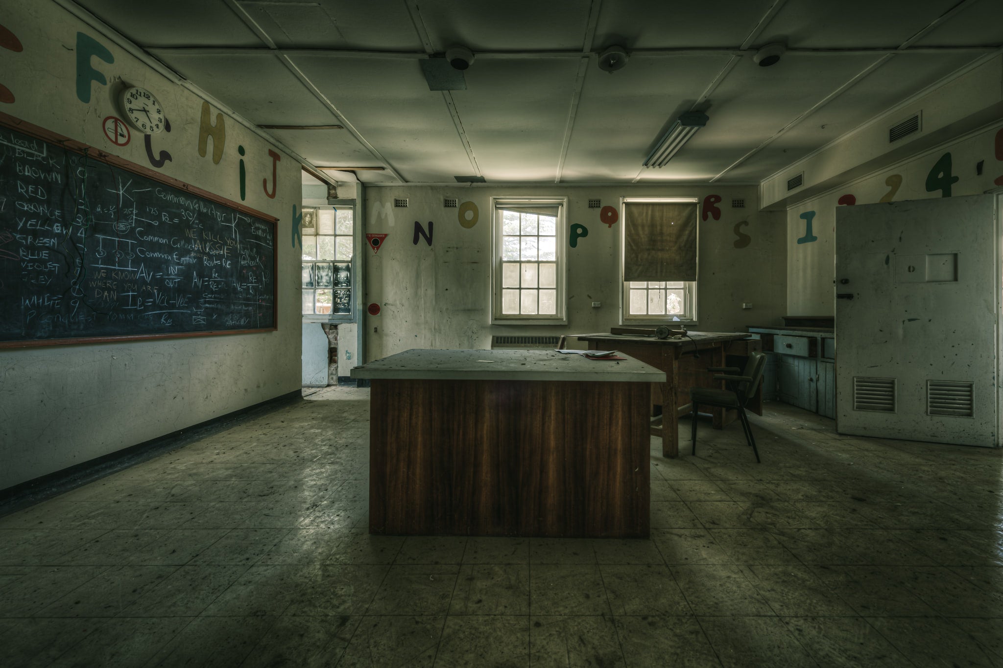 Teaching Table at The Asylum, a heavy timber desk sits at the centre of a disused classroom.
