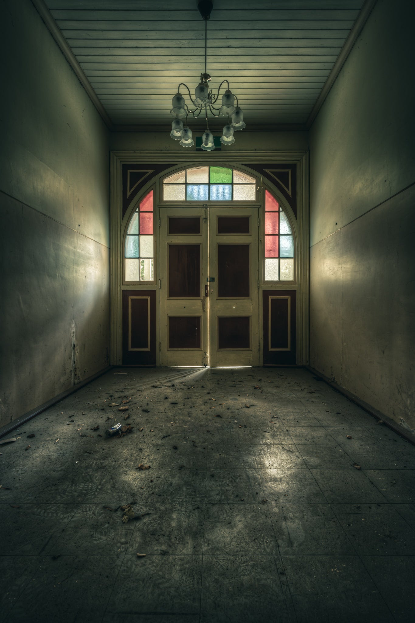 The Grand Entrance at The Asylum, a narrow entrance hall opens toward double timber doors set within an arched frame.