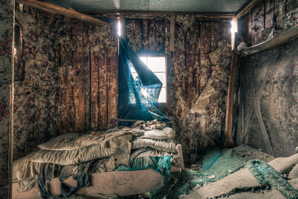 Floral at The Post Office, a torn blue curtain hangs from a window, half-collapsed, letting a shaft of light cut.