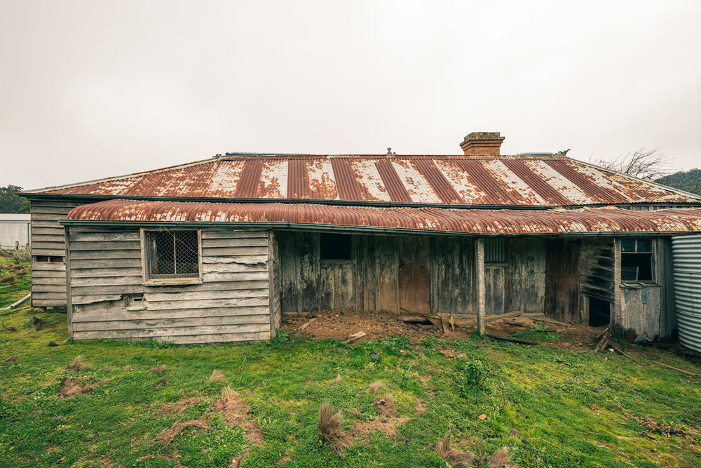 Front Yard at The Post Office, a low-slung timber homestead sits under a corrugated iron roof mottled with rust.