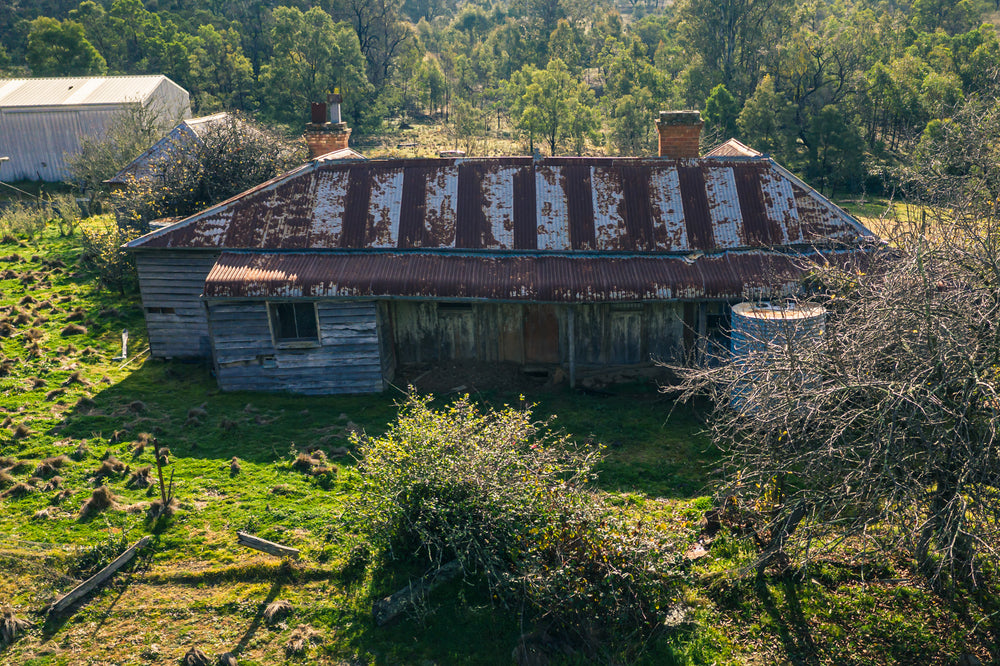 Frontside Elevated at The Post Office, a weatherboard homestead sits low against green pasture, seen from above.