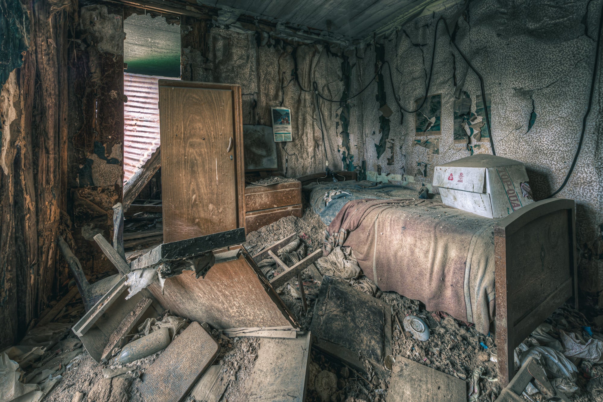 Life As It Was at The Post Office, a single bed sits against the back wall, a faded pink blanket still draped.