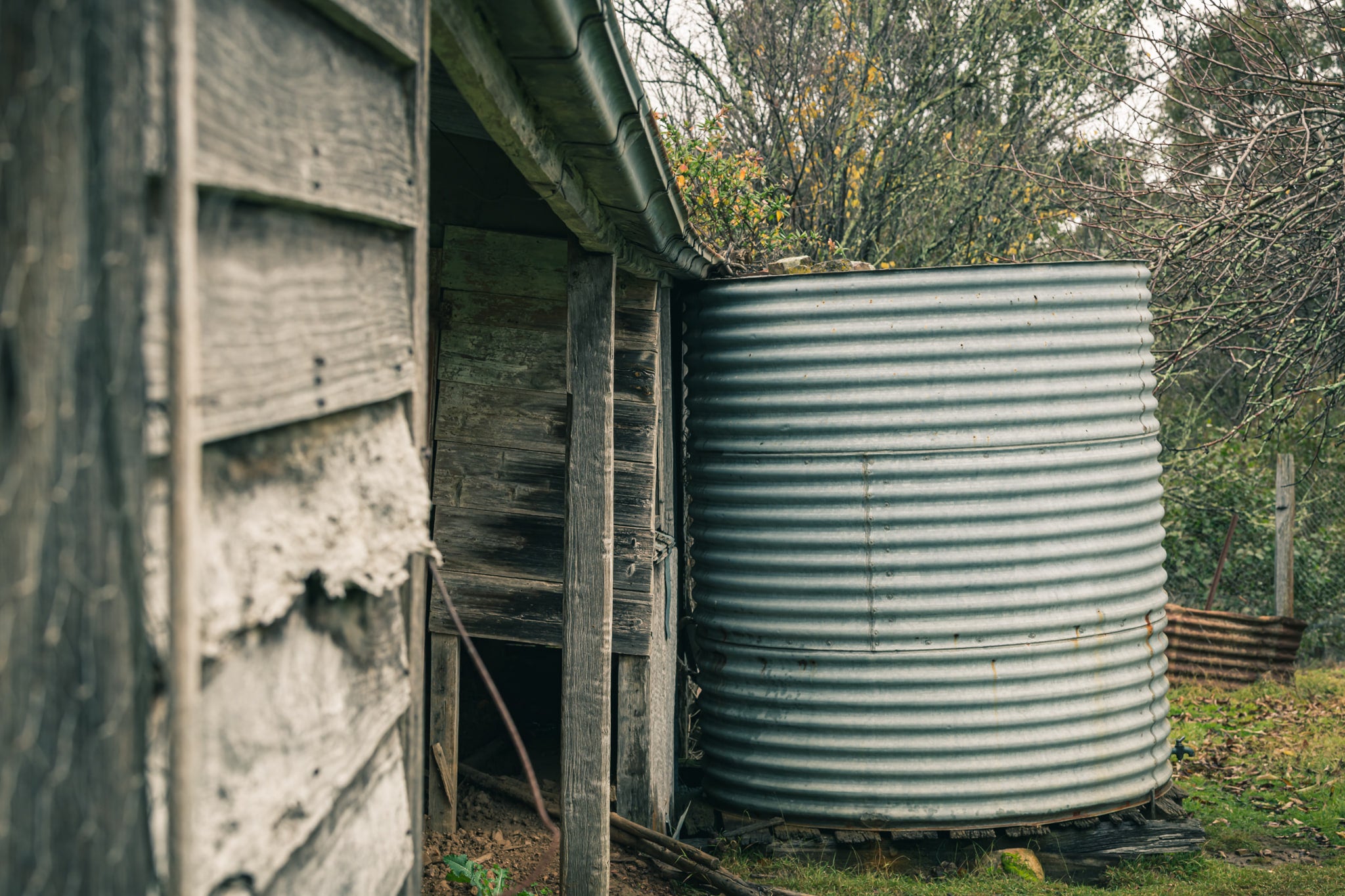 Water Tank at The Post Office, a corrugated steel water tank sits tight against the back corner of a timber outbuilding.