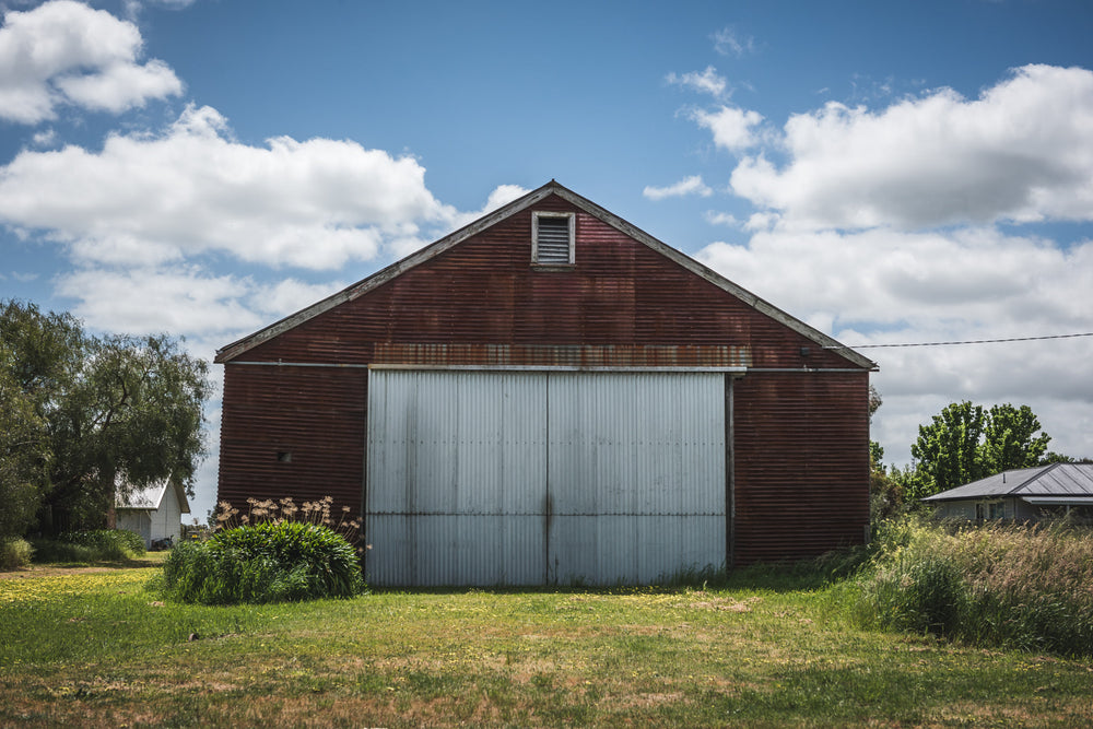 Colac Garden Shed at The Woolshed, a corrugated iron shed sits square to the frame, its walls stained deep rust-red.