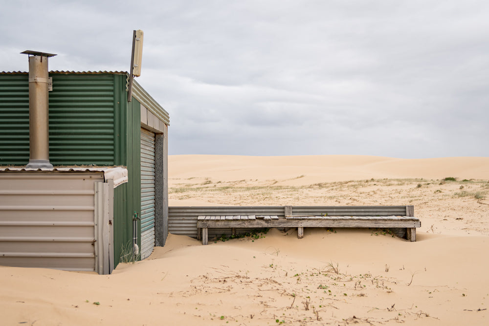 Boardwalk at Tin City, a corrugated iron shack sits half-buried in sand.