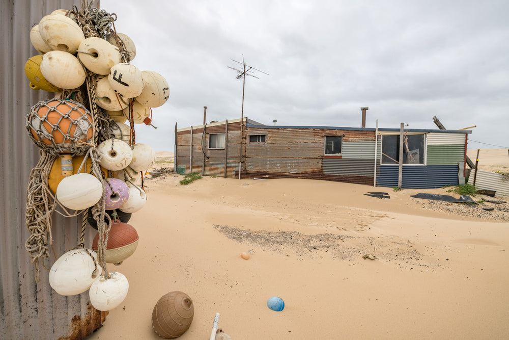 Buoys at Tin City, a cluster of fishing buoys hangs from a corrugated iron wall.