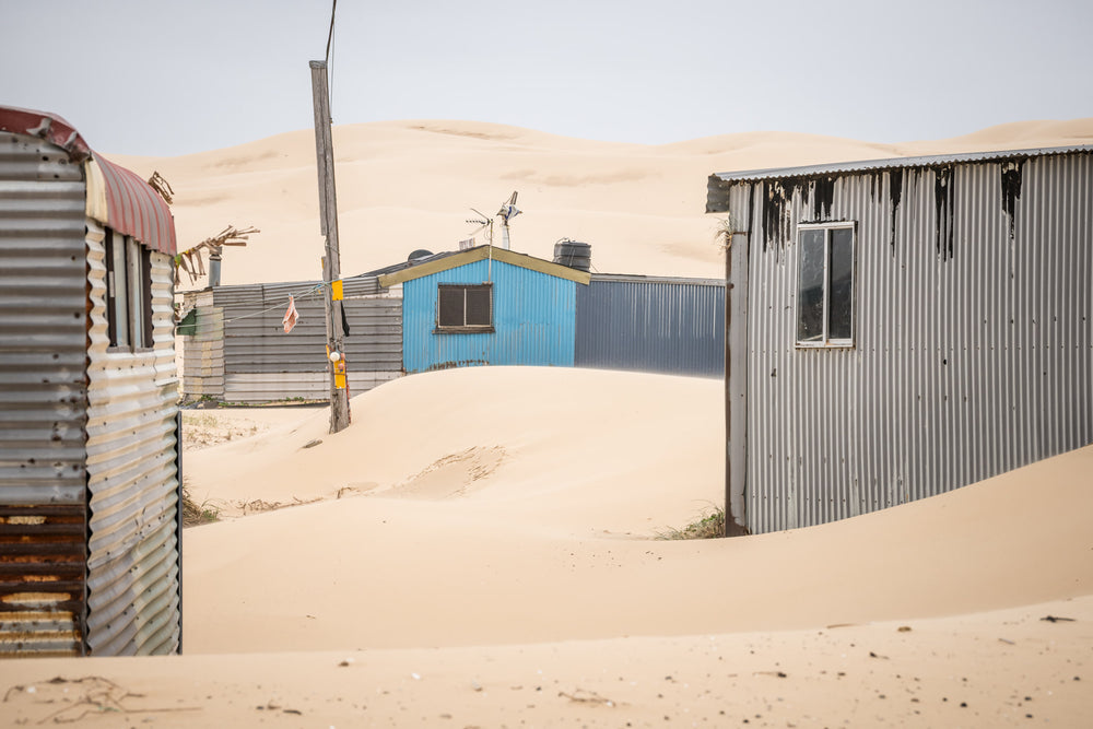 City Centre at Tin City, sand drifts between corrugated iron shacks, banking against walls in smooth curves.