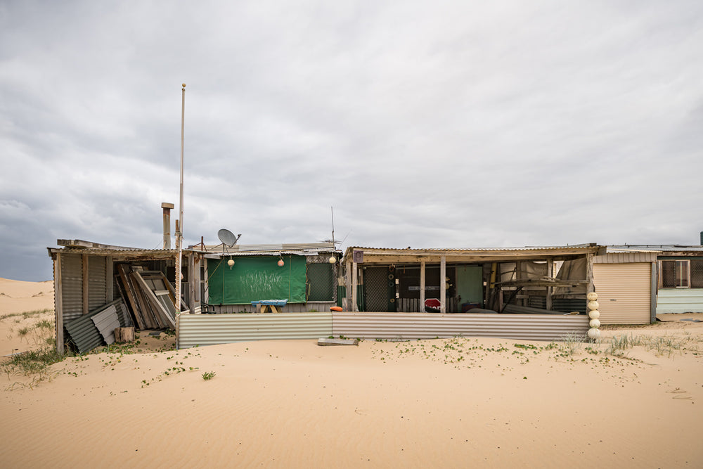 Nine at Tin City, corrugated iron and shade cloth hold together a low sprawl of shack against the dunes.