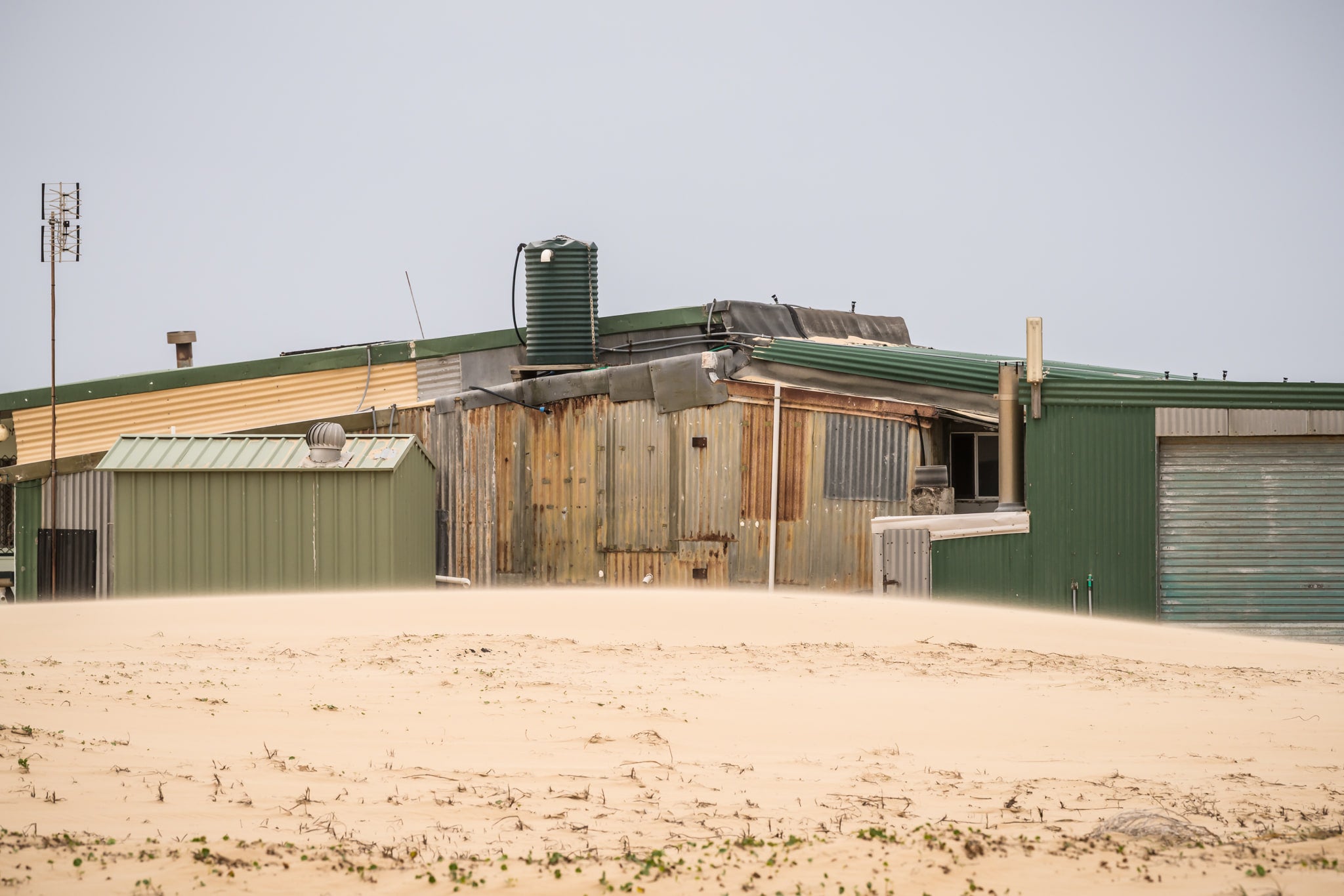 Patchwork at Tin City, green and rust-brown corrugated iron panels sit side by side across a long, low structure.