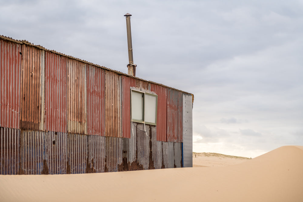 Red Walls at Tin City, corrugated iron panels in rust red, faded salmon, grey and bare steel form the wall of a shack.