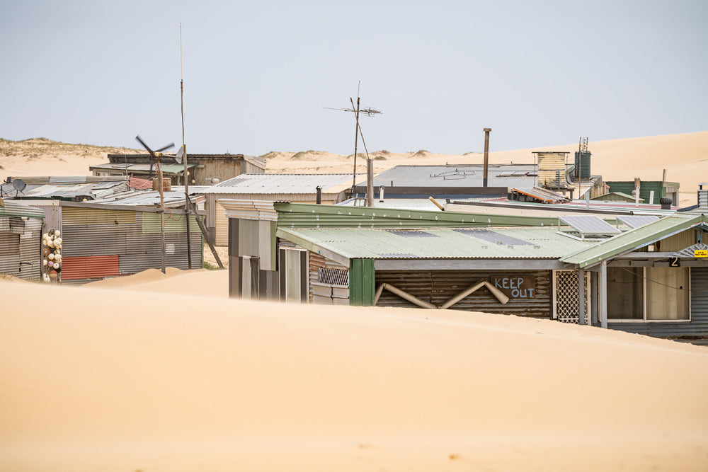 Rooftops at Tin City, sand rises to the rooflines of a cluster of makeshift shacks at Tin City.