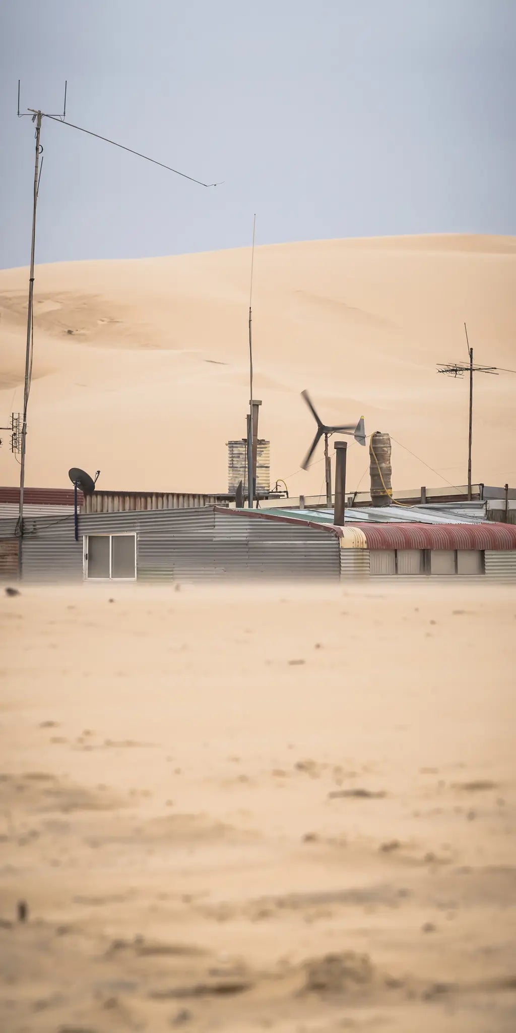 Tin City huts nestled in the rolling sands of Stockton Dunes, an isolated community framed by the stark beauty of the desert landscape.