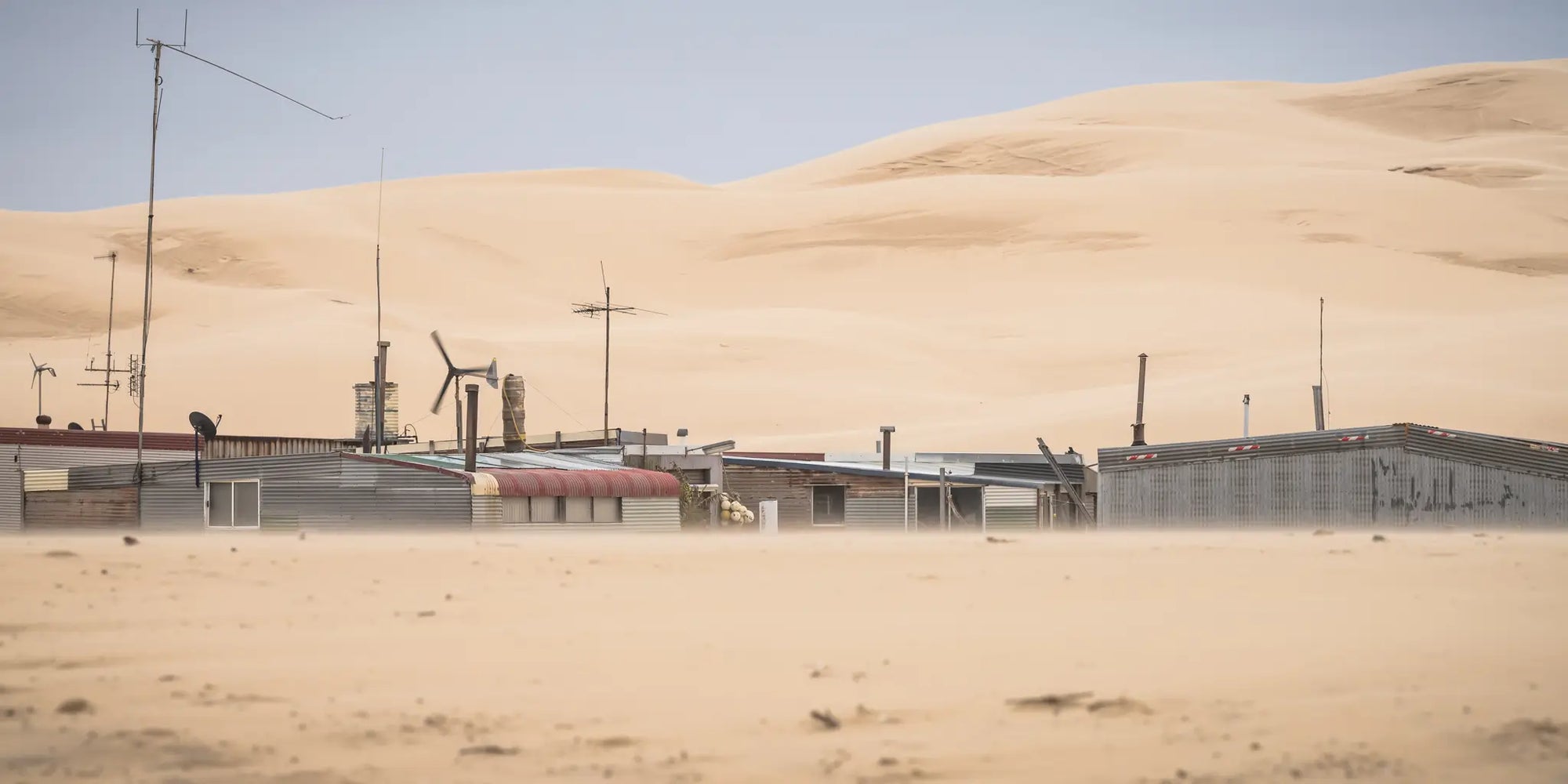 Tin City huts nestled in the rolling sands of Stockton Dunes, an isolated community framed by the stark beauty of the desert landscape.