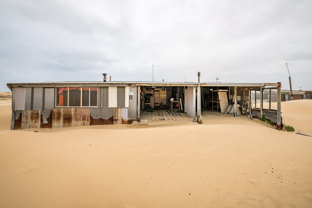 The Garage at Tin City, sand presses against the lower walls of a long, low shack at Tin City.