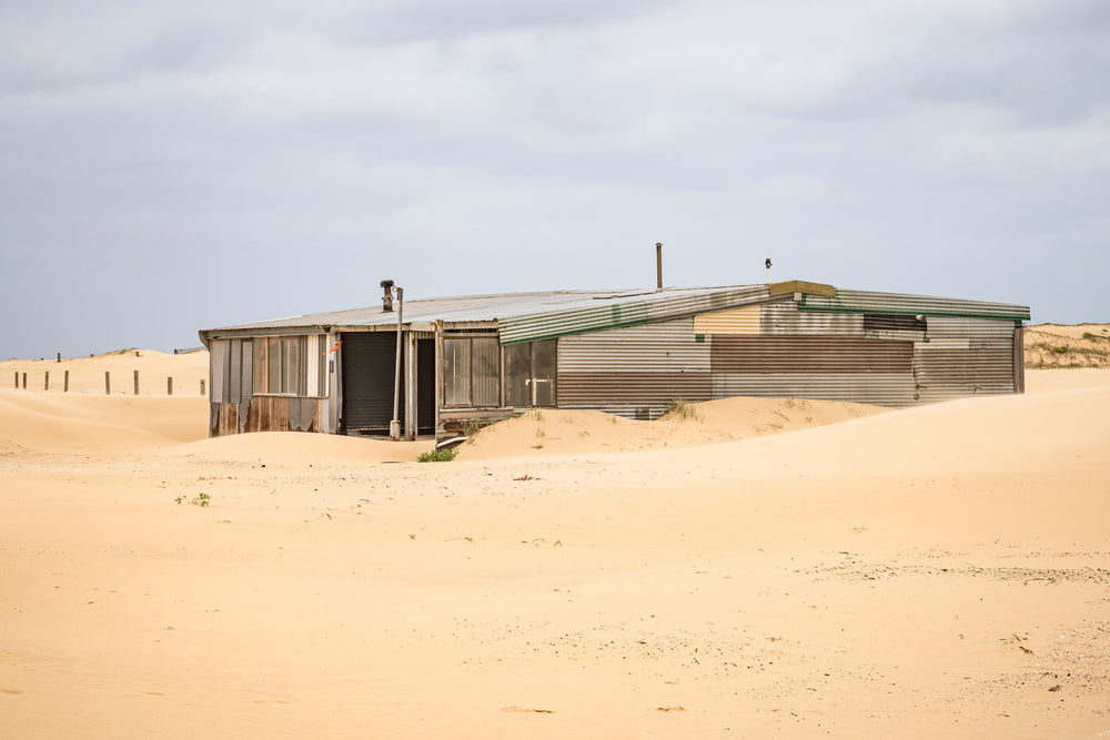 The Workshop at Tin City, a low corrugated iron structure sits half-swallowed by sand dunes at Tin City.