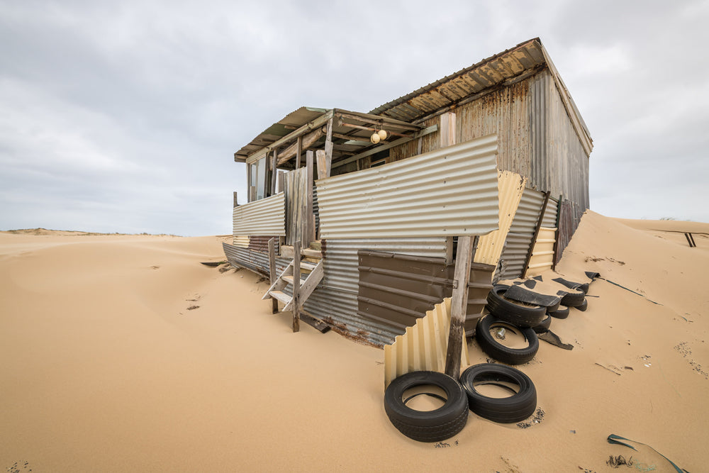 Tyres at Tin City, a corrugated iron shack lists sideways into a dune, its verandah posts leaning at odd angles.
