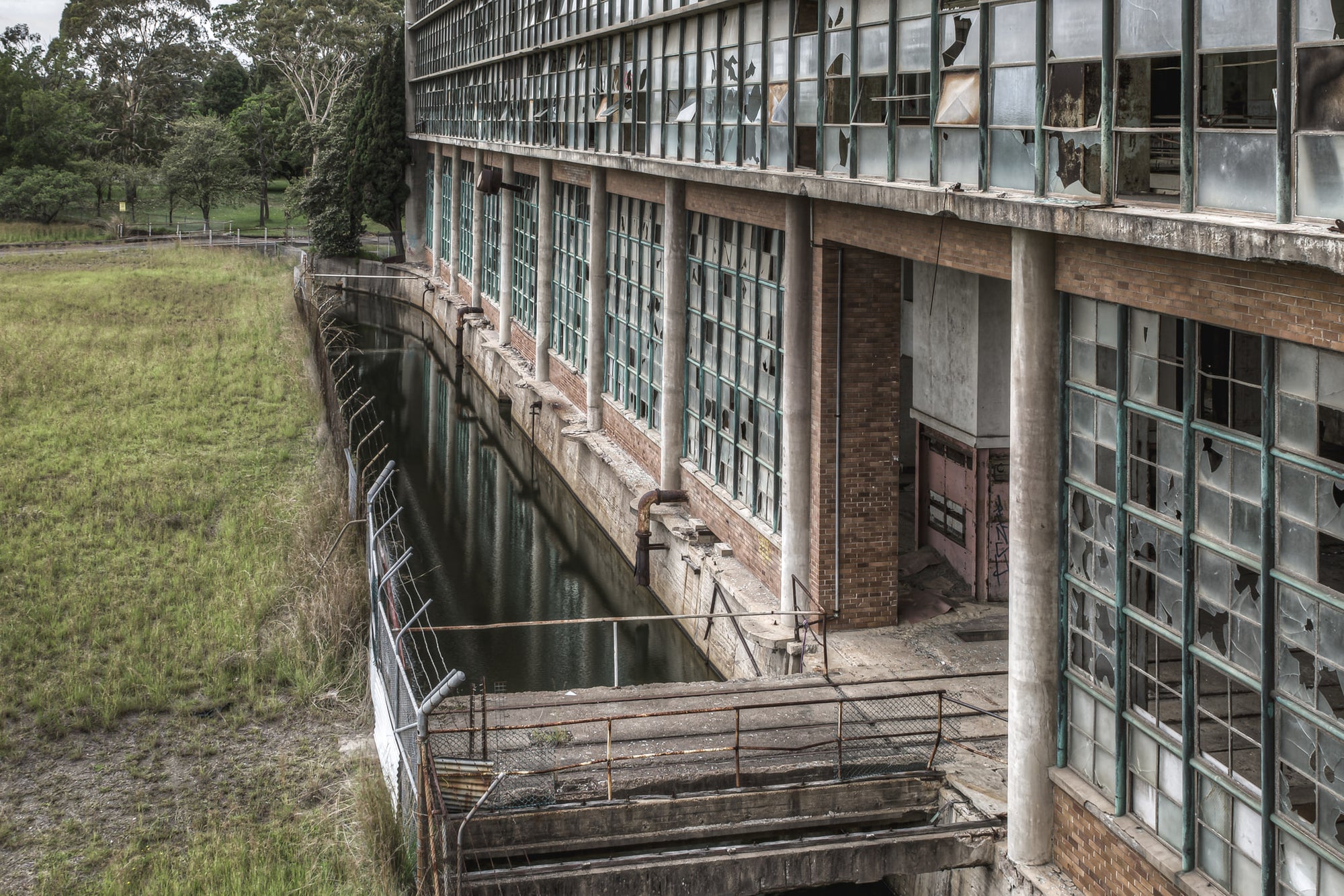 Outlet Canal at Wangi Power Station, brown brick and steel-framed windows rise two storeys above, nearly every pane.