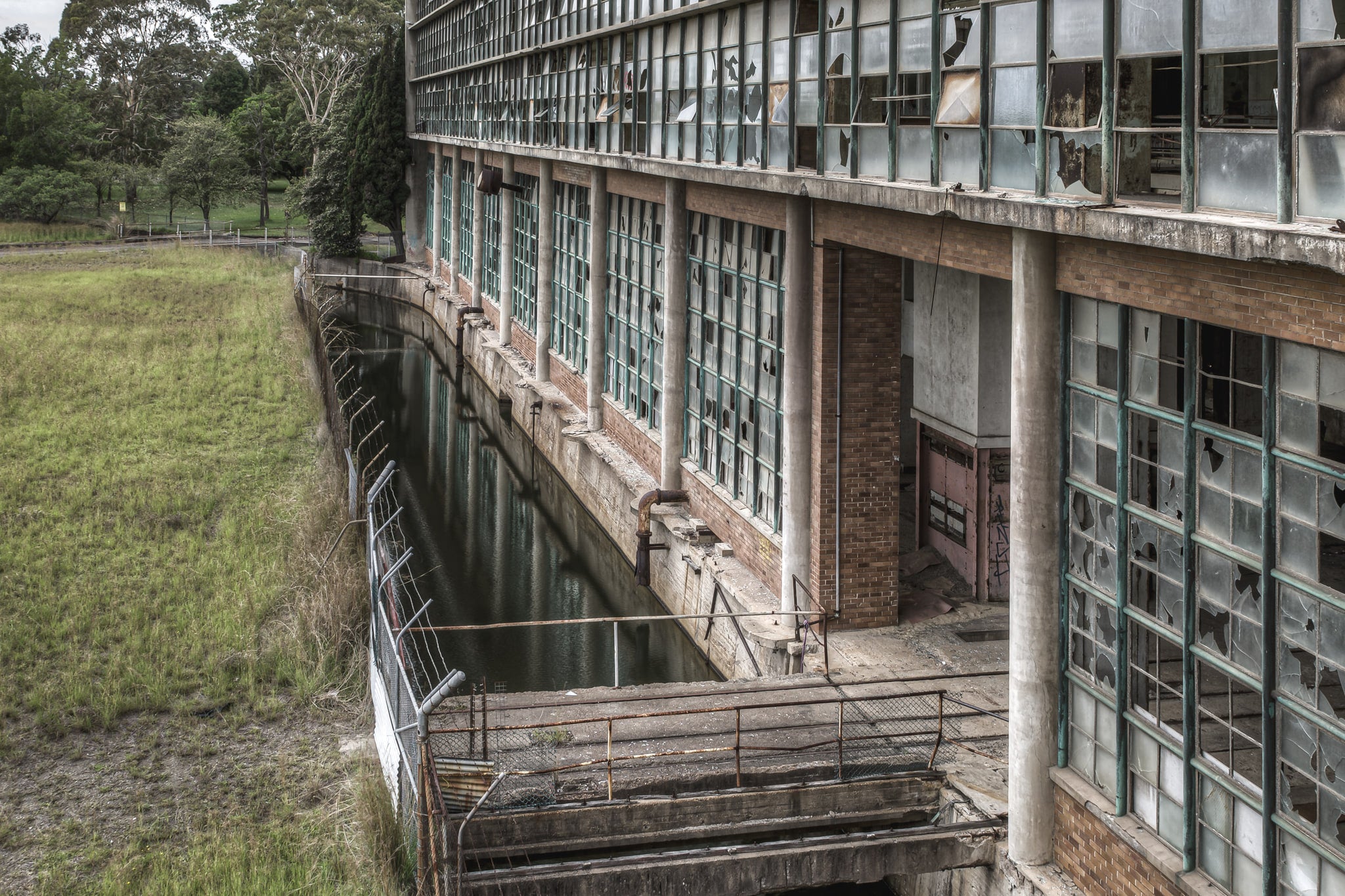 Outlet Canal at Wangi Power Station, brown brick and steel-framed windows rise two storeys above, nearly every pane.