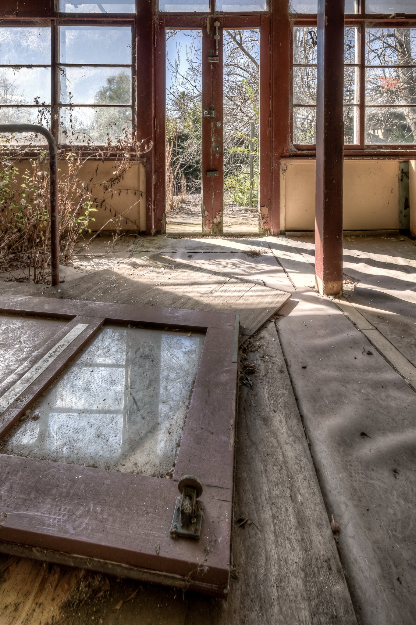 Breaking Down The Doors at Waterfall Sanatorium, a timber door lies flat on the floorboards, its glass panel still intact.