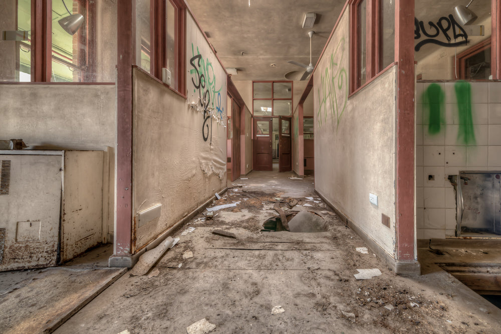 Fallen Through at Waterfall Sanatorium, a corridor runs between partitioned rooms, their maroon-trimmed frames holding.