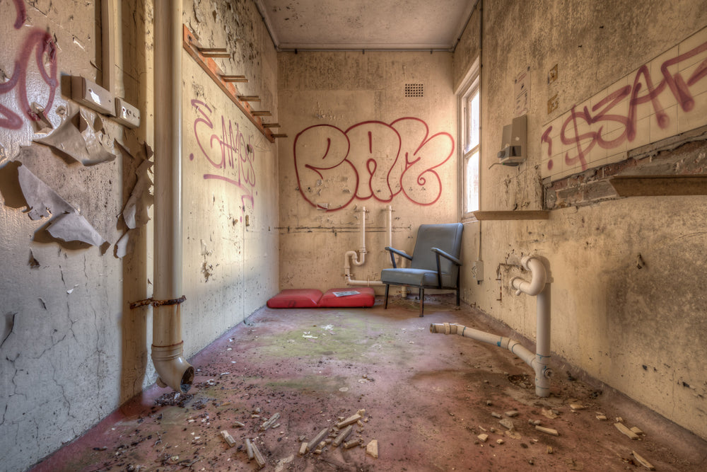 Laundry at Waterfall Sanatorium, a blue vinyl chair sits beneath a window in a narrow room.