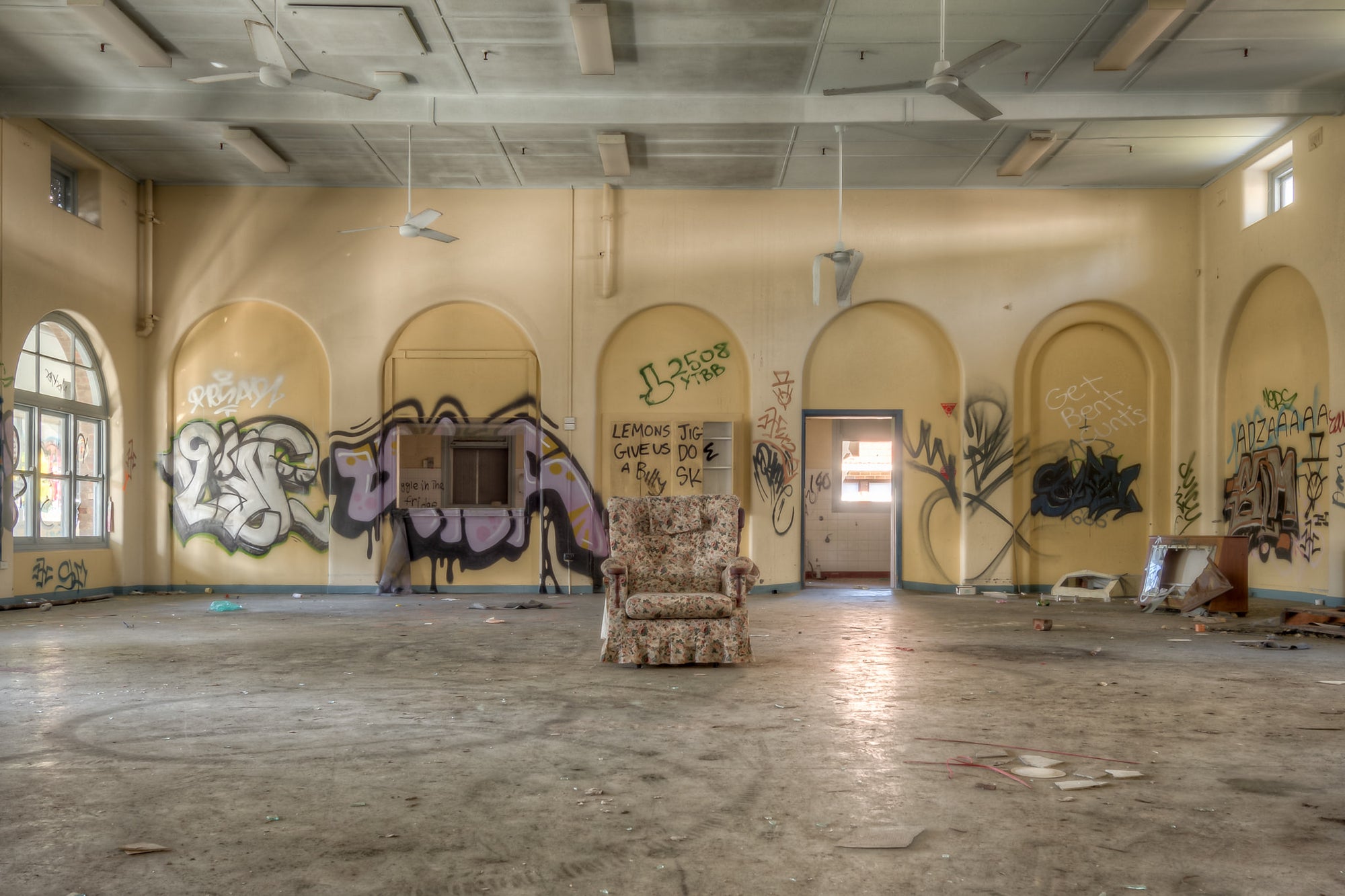 Lone Chair at Waterfall Sanatorium, a floral armchair sits alone at the centre of a large hall.