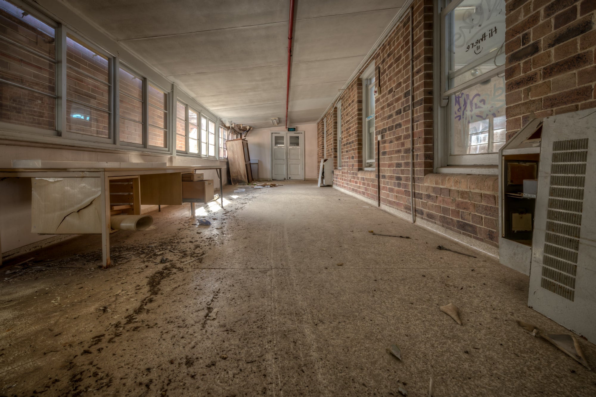 Marbled Lino at Waterfall Sanatorium, a long corridor runs between a brick interior wall and a row of louvred windows.
