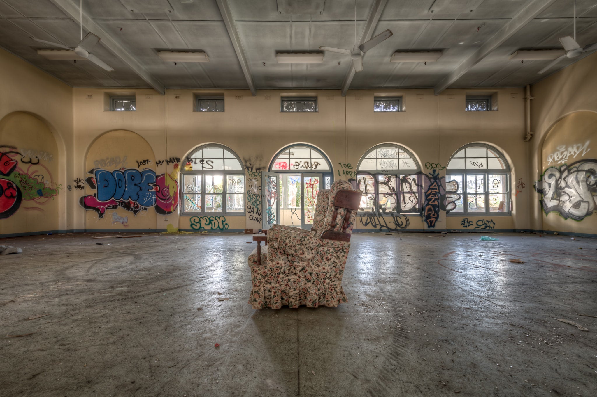Side Chair at Waterfall Sanatorium, a floral armchair sits alone at the centre of a large hall.