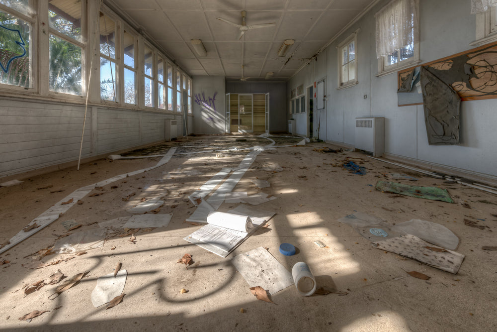 Sprawl at Waterfall Sanatorium, sunlight falls through a long bank of windows onto a debris-covered floor.