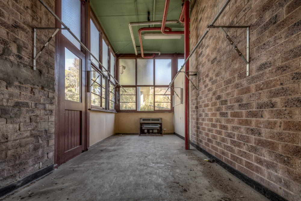 The Side Room at Waterfall Sanatorium, a narrow brick corridor leads toward a wall of steel-framed windows.