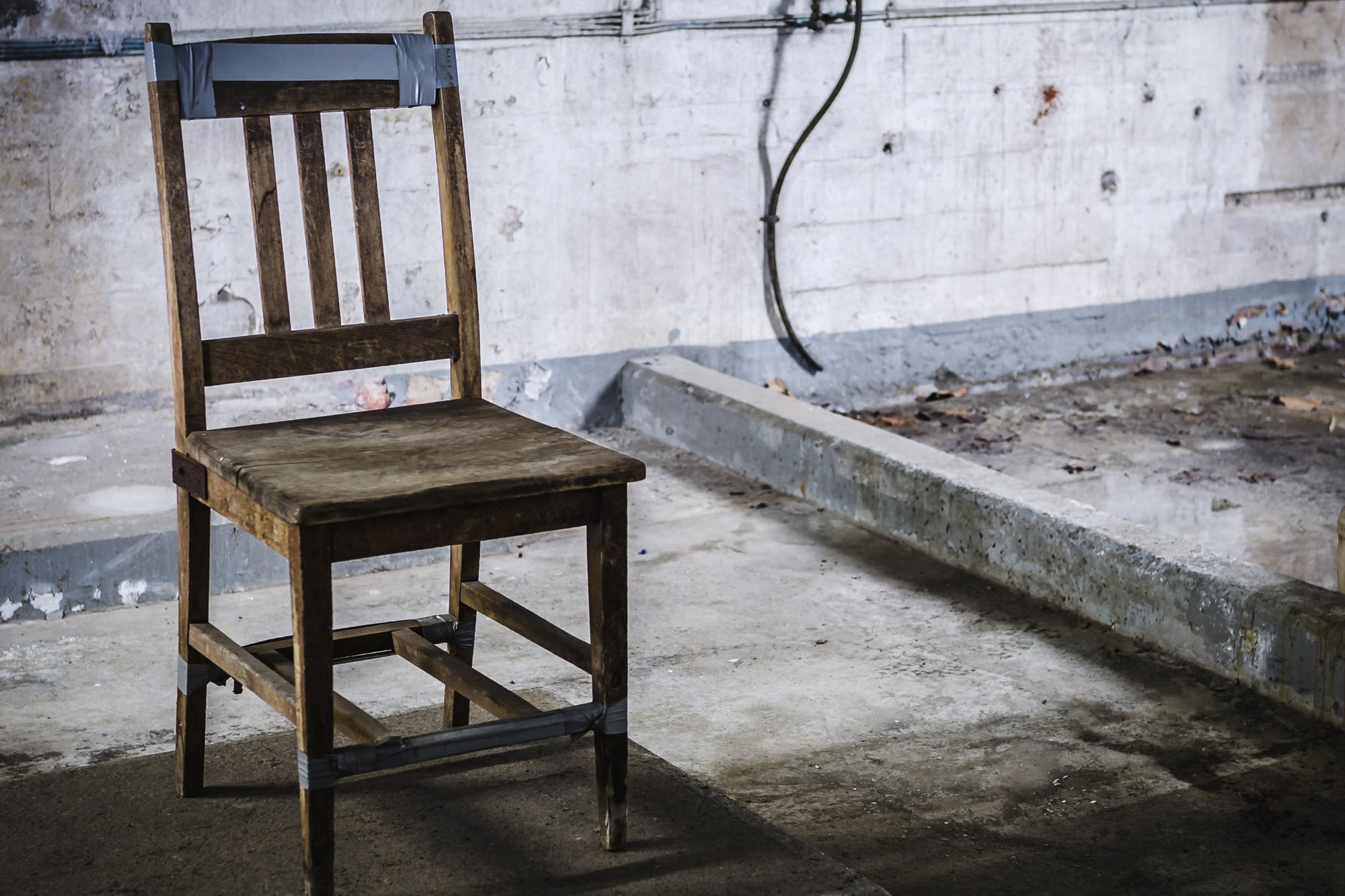 Chair at West Ryde Pumping Station, a wooden chair sits on a bare concrete floor, held together with strips of grey duct.