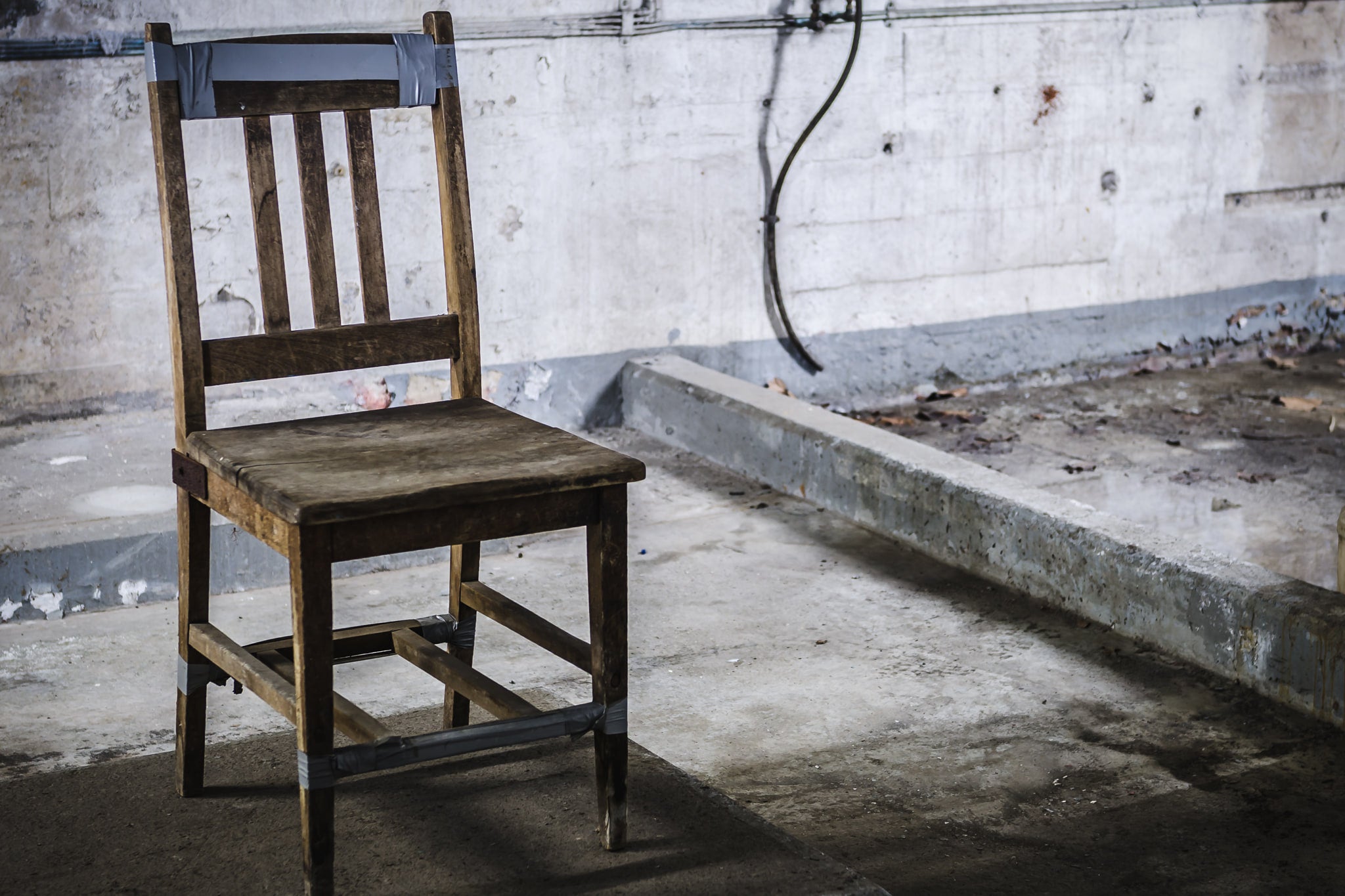 Chair at West Ryde Pumping Station, a wooden chair sits on a bare concrete floor, held together with strips of grey duct.