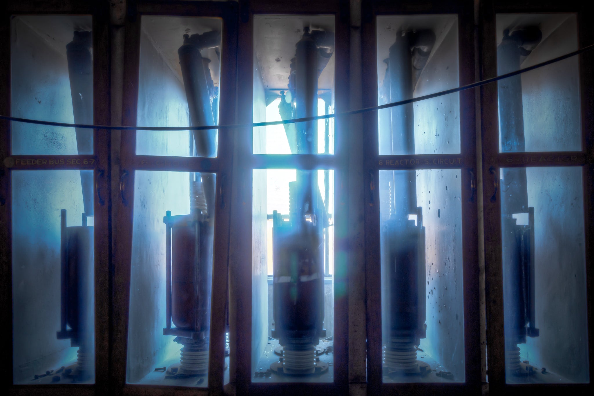 Backlit Reactors at White Bay Power Station, high-voltage reactor switches stand in glass-panelled enclosures, backlit.