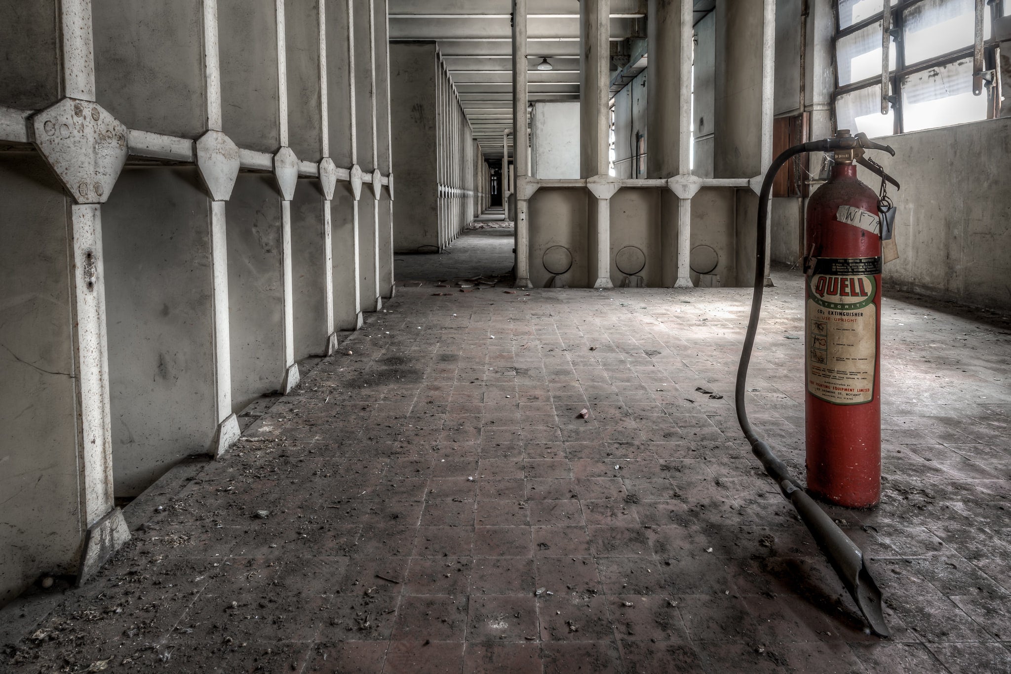 Fire Extinguisher at White Bay Power Station, a red Quell fire extinguisher stands on a grime-covered brick floor.