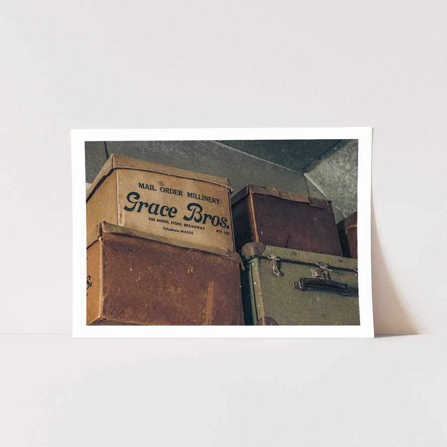 Grace Bros. hatboxes stacked beside a green canvas suitcase with metal latches and a leather handle, photographed at Moruya.