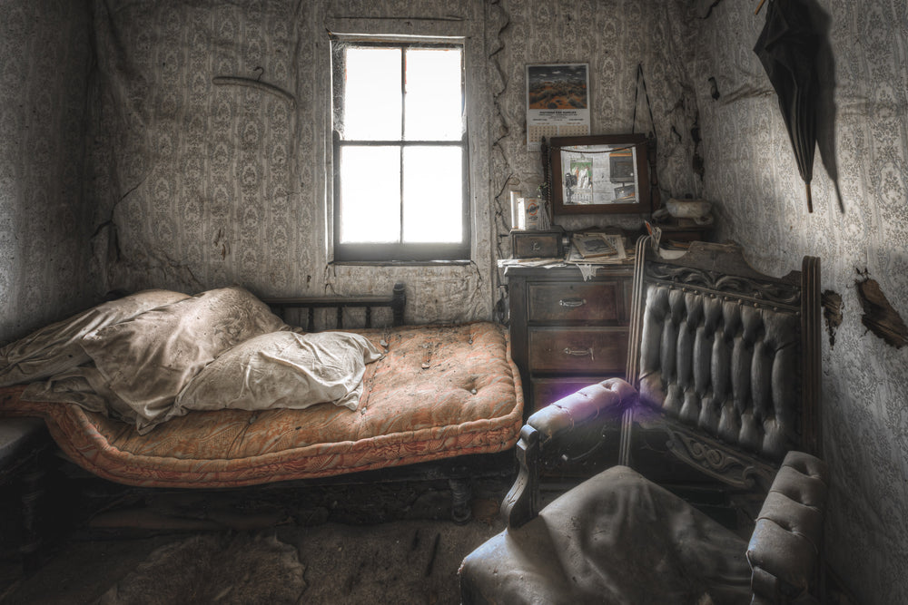 Side Bedroom Window at Woolla, a single iron-frame bed sits against the far wall, its faded orange mattress still bearing.