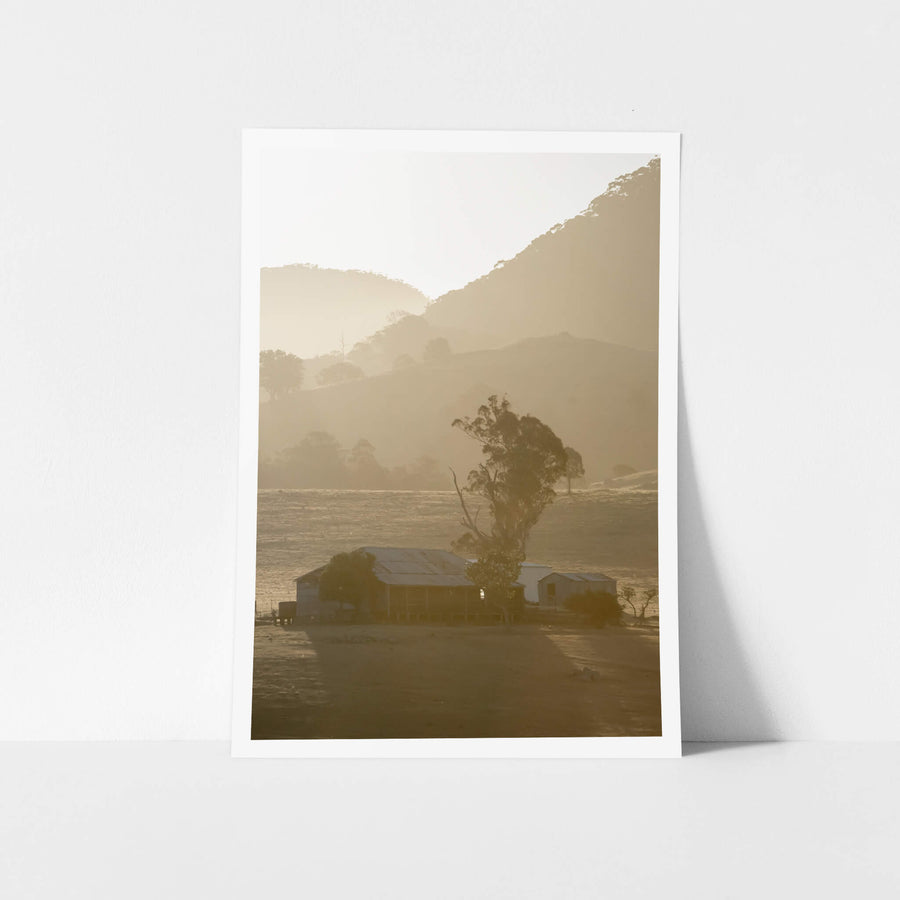 Farmstead at A Place to Call Home, a corrugated iron homestead and outbuildings sit low on bare ground, flanked by a single.