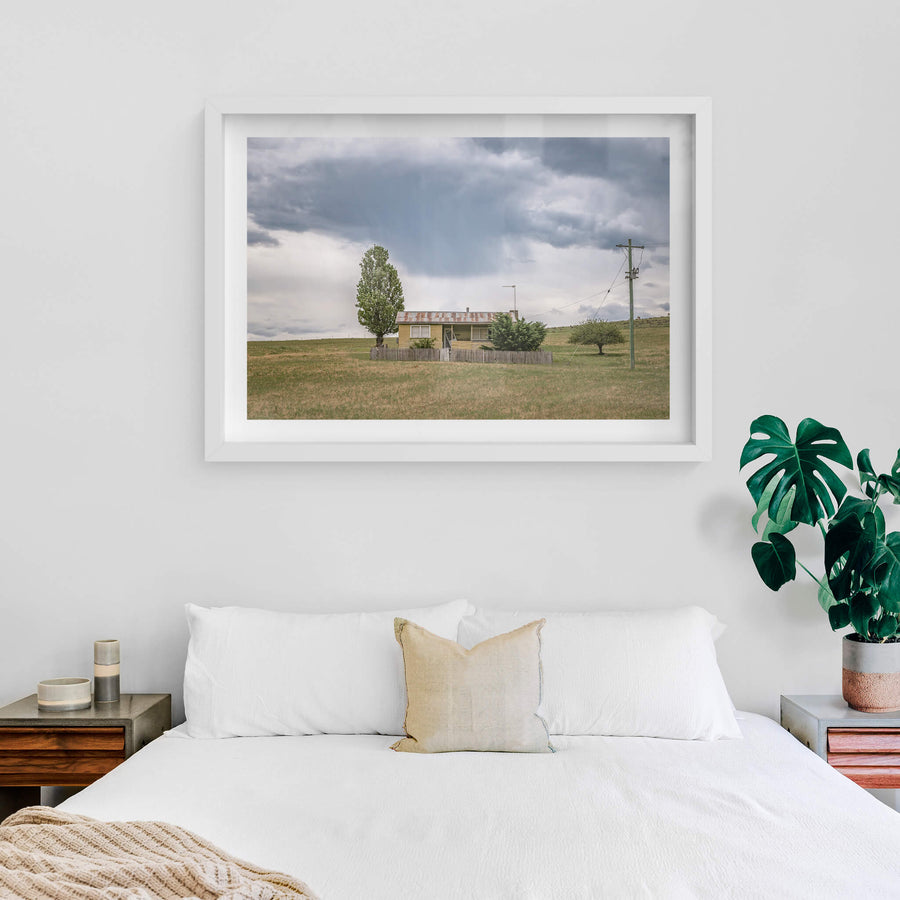 Home On the Range at A Place to Call Home, a long-vacant, lone farm cottage sits in a field beneath a distant rain cloud.