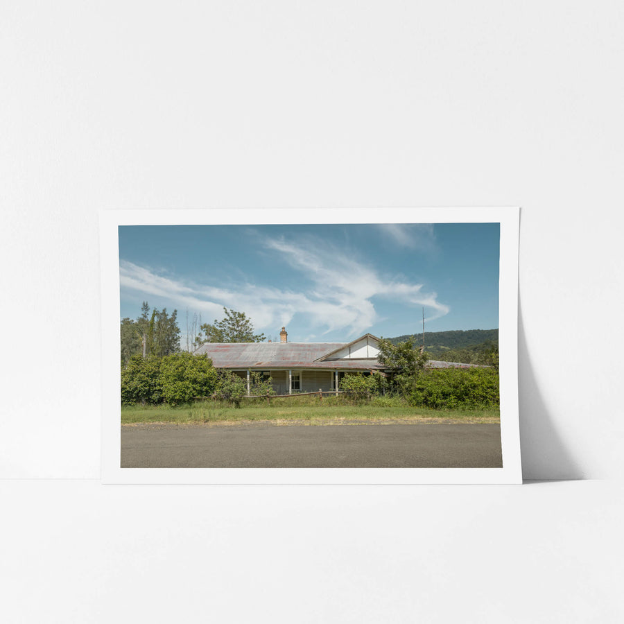 Hunter Hiding at A Place to Call Home, a weatherboard farmhouse sits back from the road edge, half-swallowed by dense green.